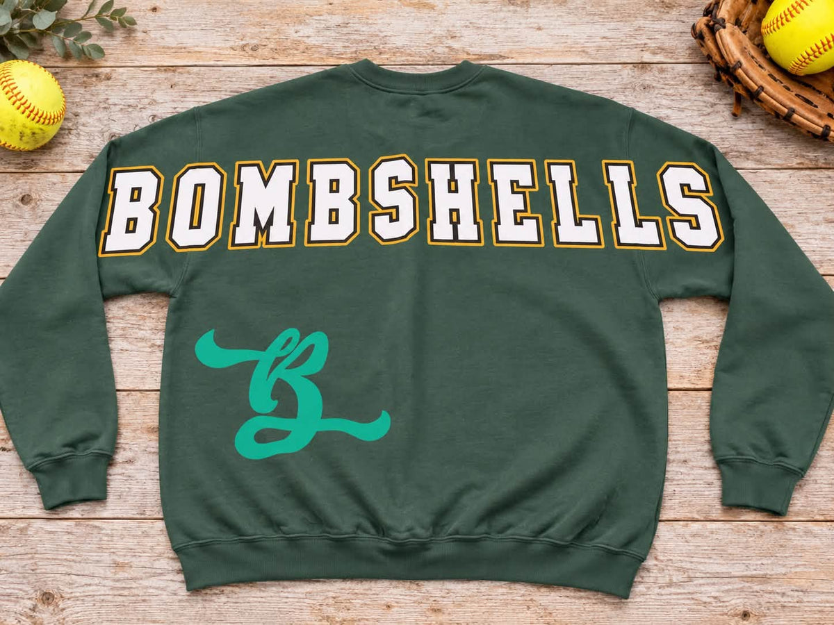 Forest green Bombshells softball crewneck sweatshirt back print with large white letters outlined gold and teal B emblem