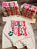 Holly Jolly colorful Christmas print on ivory shirt with folded stacks in background